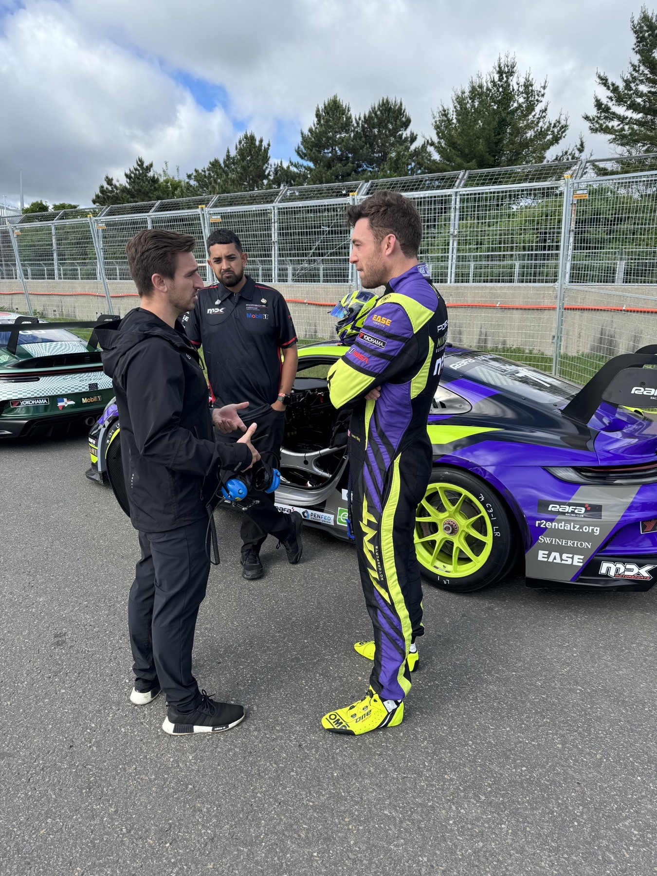 A trackside conversation beside a purple and lime Porsche race car
